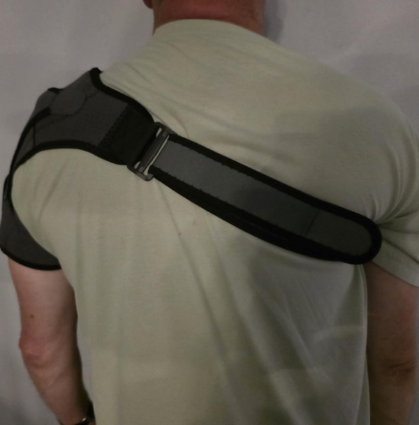 Man wearing black adjustable shoulder heating pad from the back view, showing strap and support design