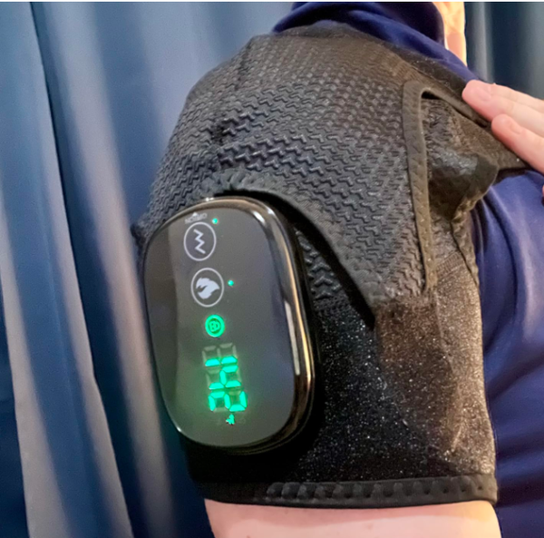 Close-up of black heated massager with glowing green digital display and control buttons on person’s shoulder/knee